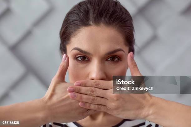 Be silent. Portrait of a sad cheerless young woman covering her mouth while being silent