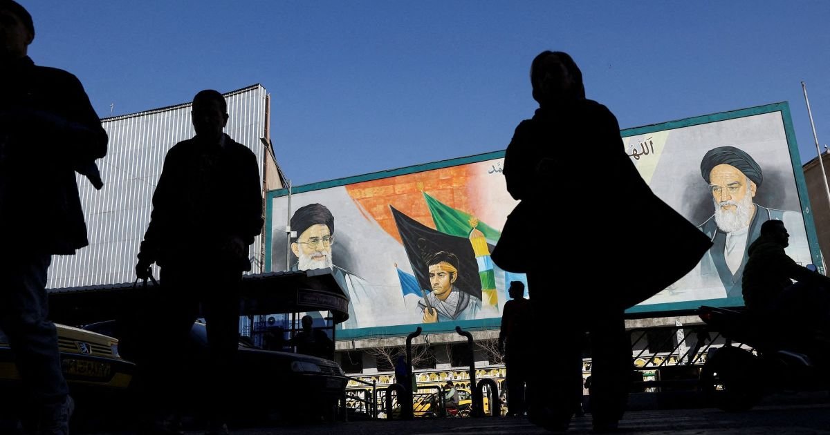 Pessoas caminham perto de um mural com imagens do líder supremo do Irã, o aiatolá Ali Khamenei...